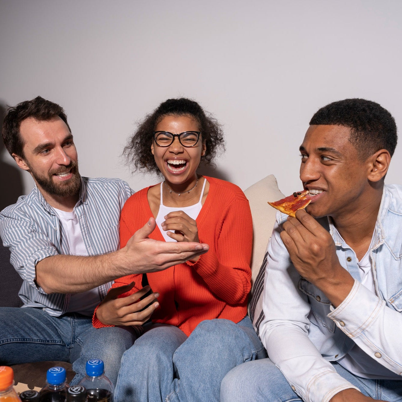 Four friends sitting together, eating pizza and laughing, with a casual setting.