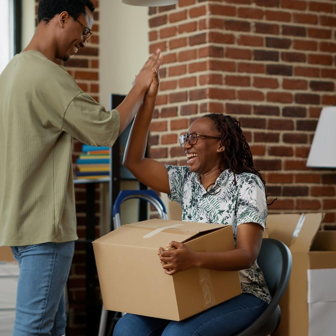 Two people in a room with cardboard boxes, high-fiving each other joyfully.