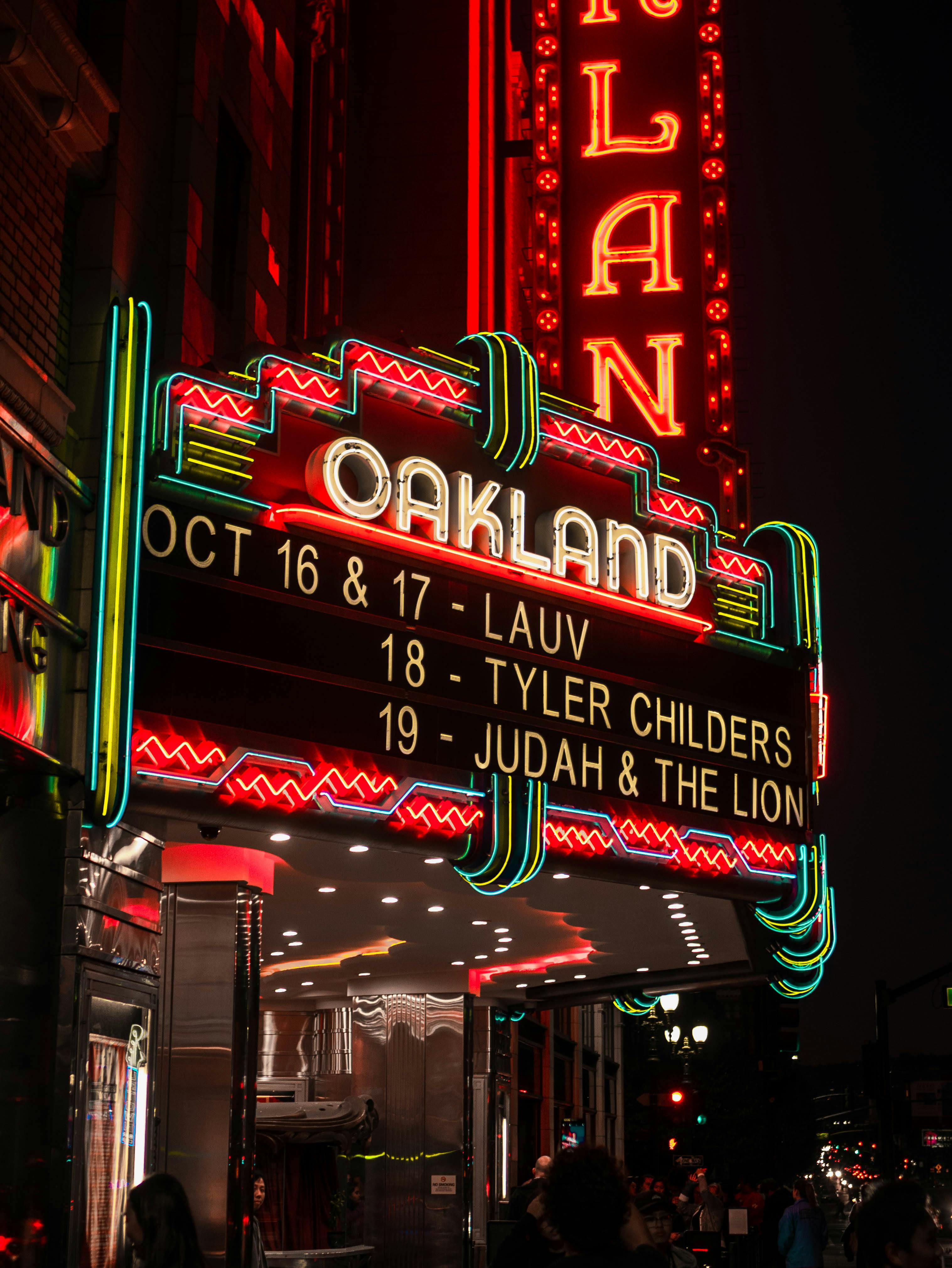 Neon sign for a concert event at night with 'Oakland' and artist names.