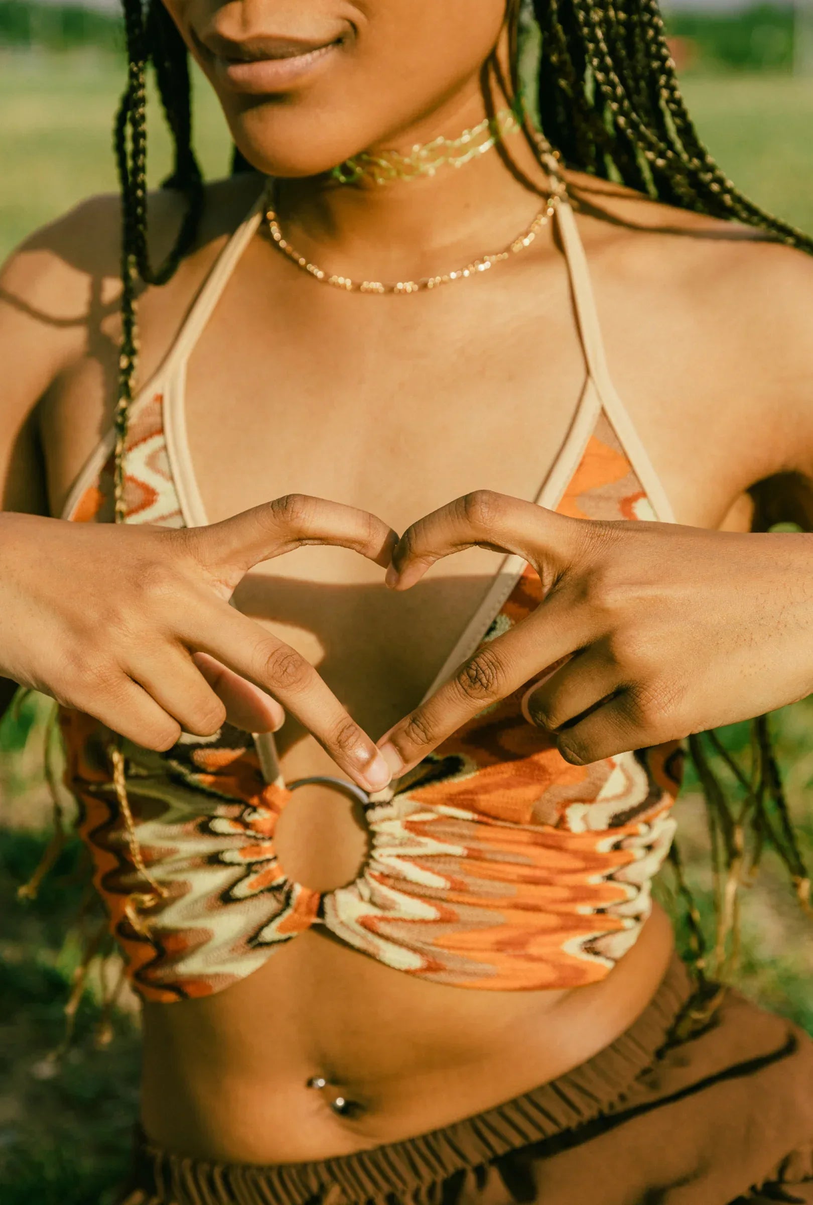 Woman wearing a colorful top and necklace, making a heart shape with her hands.
