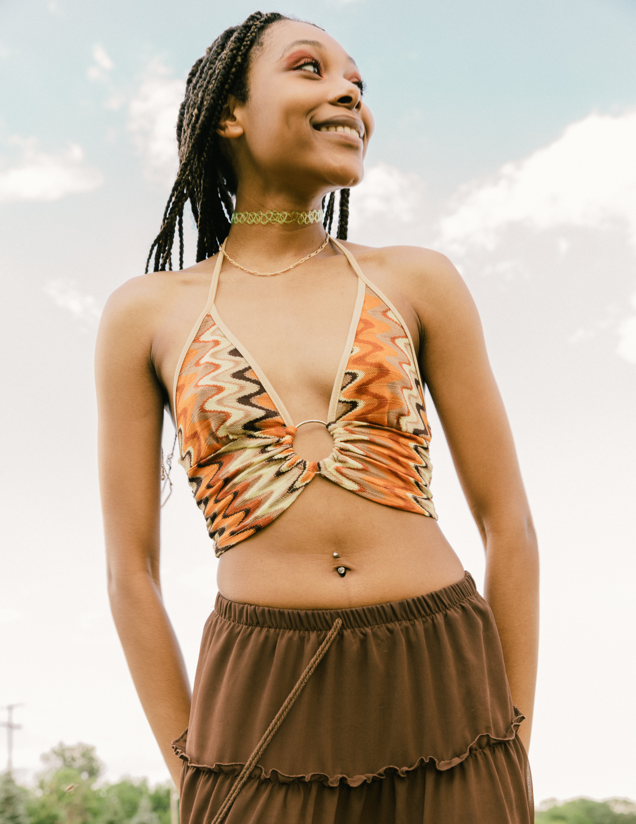 Woman wearing a patterned top and brown skirt against a sky background